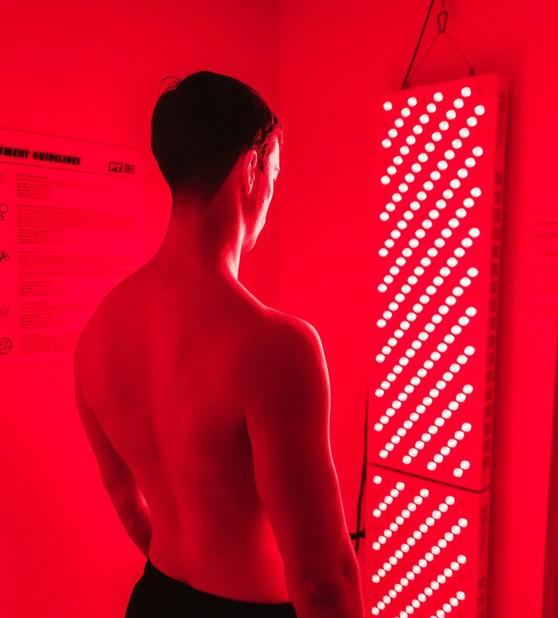 A person using a red light therapy panel on their back for muscle pain relief, with a relaxed expression and a cozy home setting.