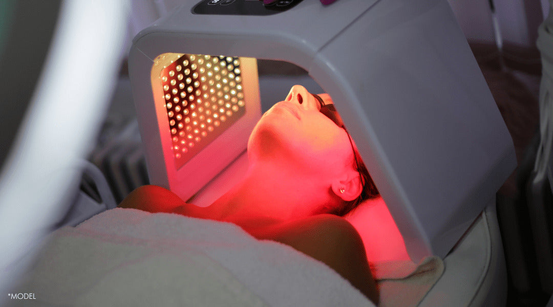 A woman using an LED light therapy mask, glowing skin visible, with different light settings targeting various skin concerns.